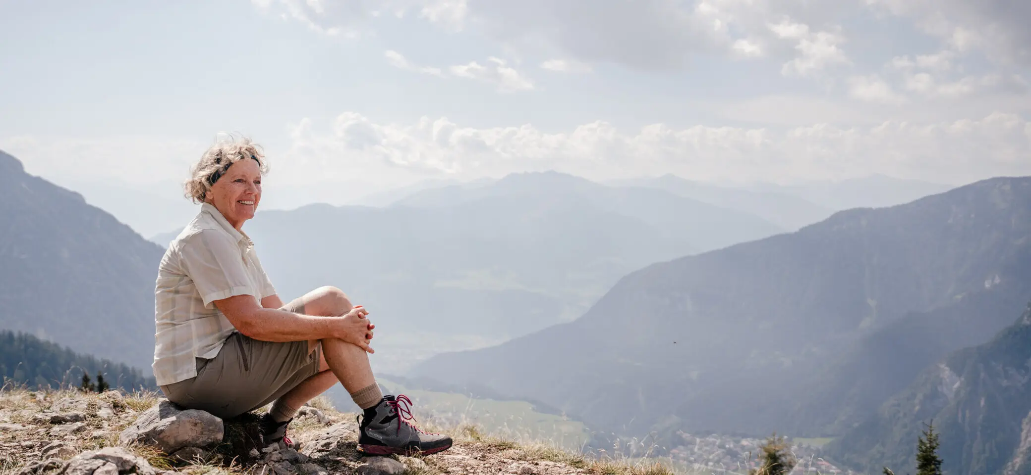 Eine ältere Dame sitzt zufrieden auf einem Felsplateau | © DAV / Marisa Koch